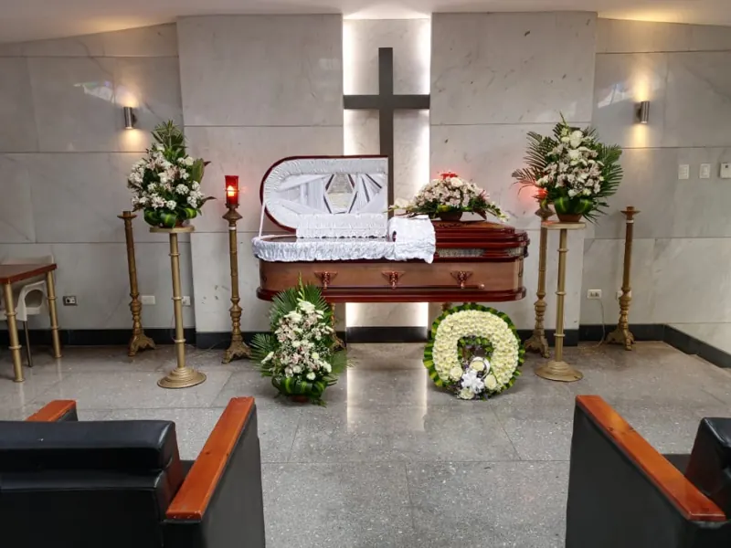 Sala velatoria con ataúd, corona fúnebre y cruz iluminada