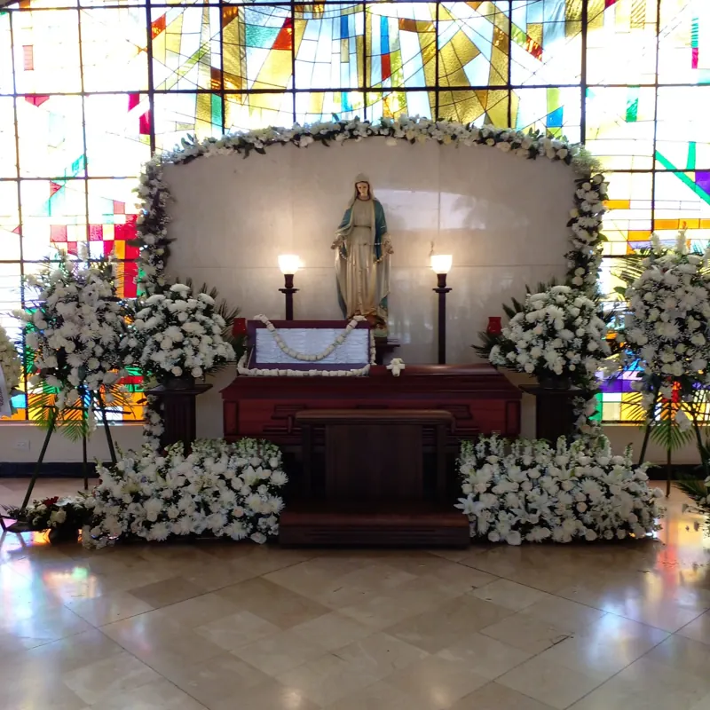 Capilla ardiente con vitral, imagen de la Virgen y flores