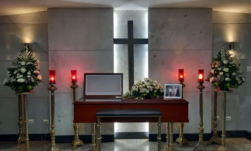 Ataúd rojo frente a cruz con velas y flores