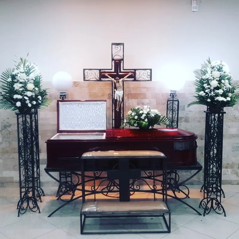 Ataúd frente a cruz de madera con arreglos florales