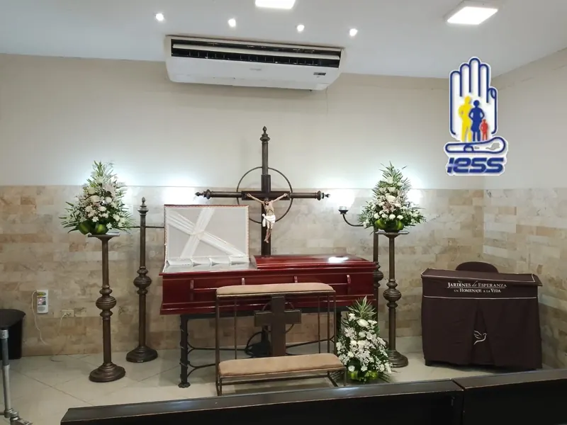 Sala velatoria con ataúd rojo y distintivo del IESS