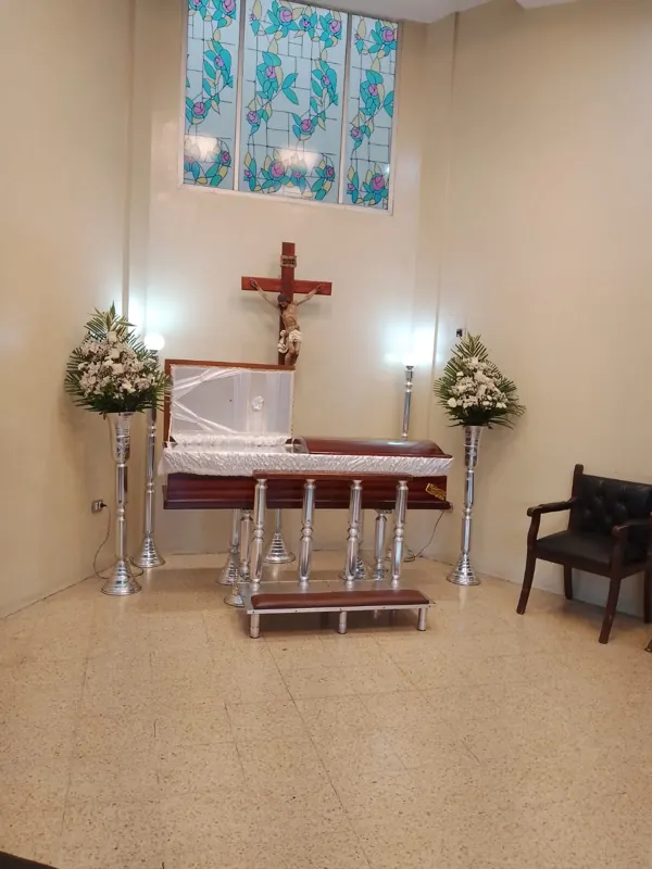 Sala velatoria con vitral, cruz y ataúd con cubierta blanca