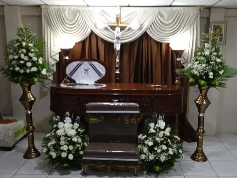 Sala velatoria con ataúd oscuro y arreglos florales blancos